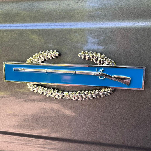 Decorative emblem with blue background and silver rifle on a metallic surface
