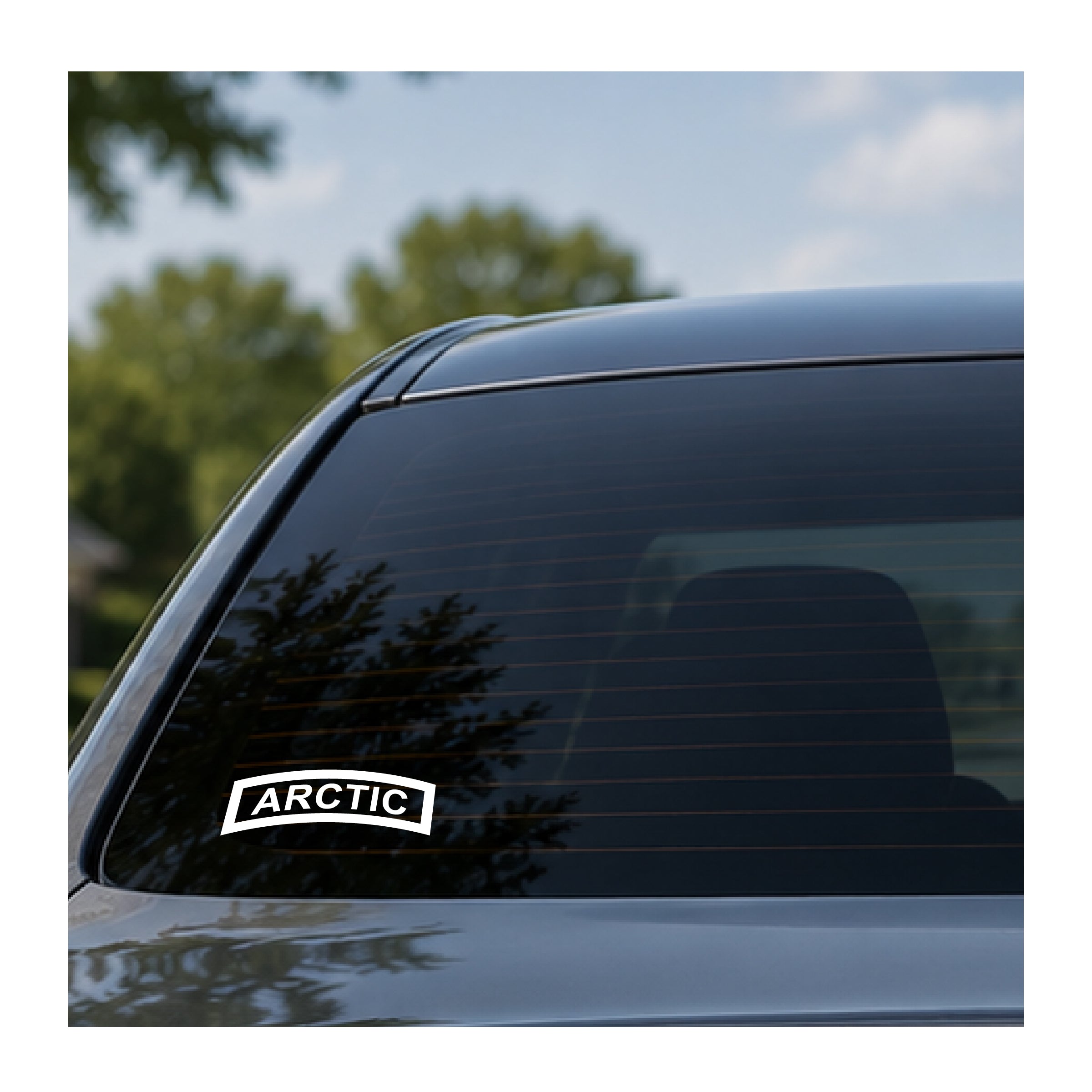 A white rectangular sticker with the word 'ARCTIC' in black letters, outlined in black, applied to the lower left of a dark tinted car window. The background shows a blurred outdoor scene with green trees and blue sky.
