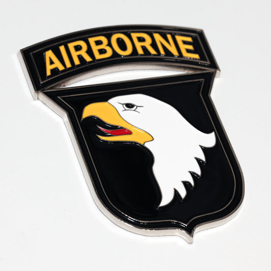 A metal patch medallion featuring an eagle and the text 'AIRBORNE' on a black background with a yellow stripe.